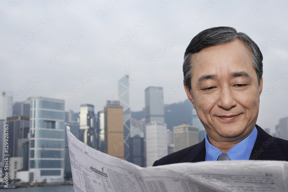 Closeup of confident middle aged businessman reading newspaper with cityscape in background Closeup of confident middle aged businessman reading newspaper with cityscape in background