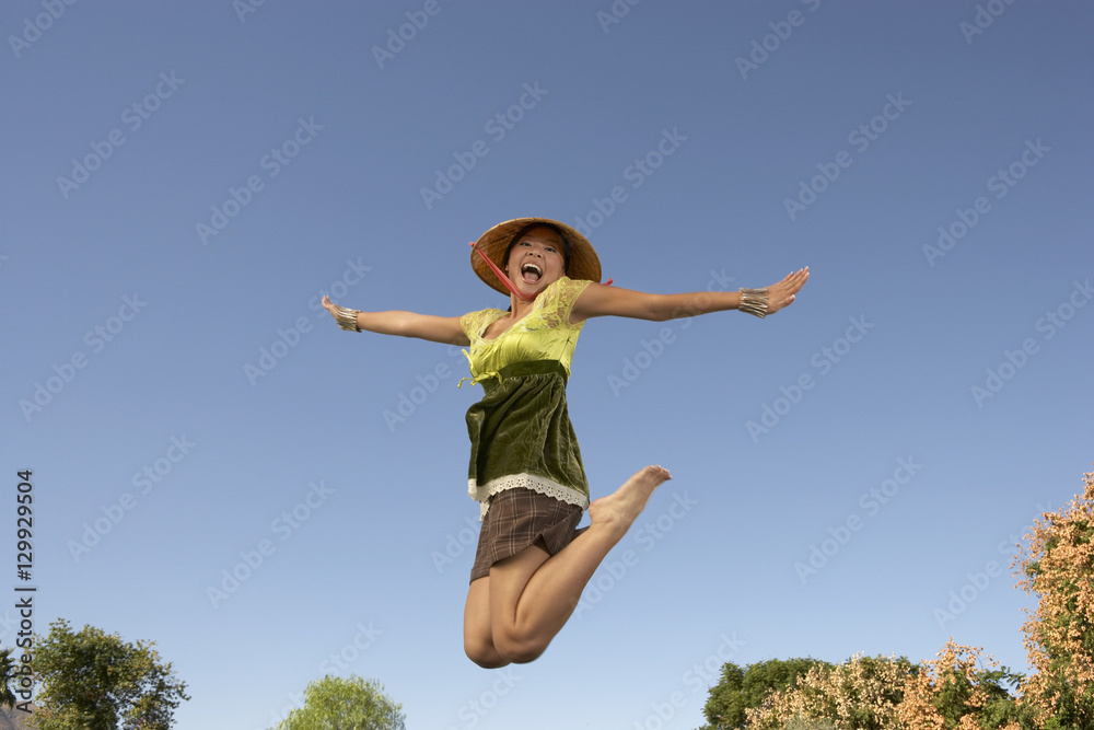 Cheerful Asian woman jumping with arms outstretched against blue sky Cheerful Asian woman jumping with arms outstretched against blue sky