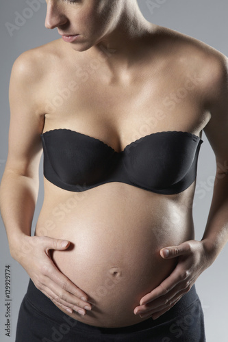 Midsection of pregnant woman touching belly on gray background