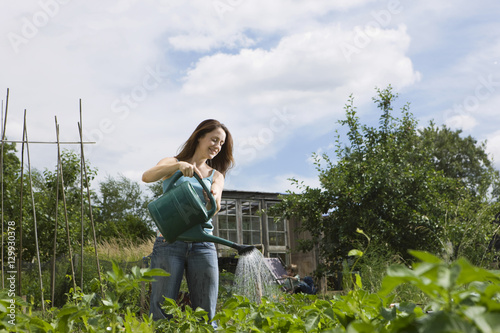 Happy woman watering plants in allotment with son in background