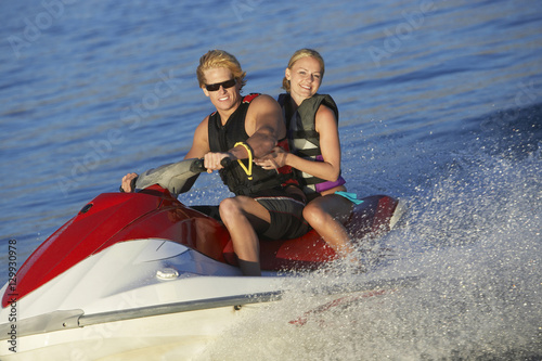 Portrait of a happy young Caucasian couple riding personal watercraft on lake