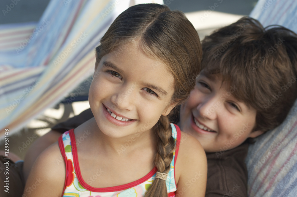 Portrait of a happy brother and sister smiling together while relaxing on deckchair Portrait of a happy brother and sister smiling together while relaxing on deckchair