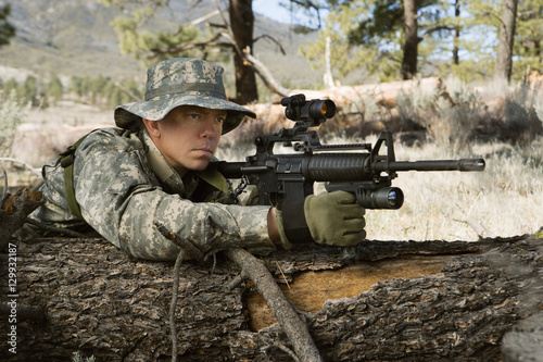 US army solider aims machine gun while leaning on log