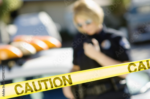 Closeup of yellow caution tape with female police officer in the background