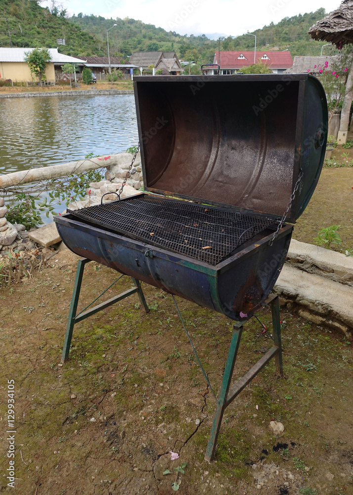 Rusty brazier with a cover for barbecue charcoal grill and green lawn in the background Rusty brazier with a cover for barbecue charcoal grill and green lawn in the background