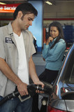 Businesswoman looking at gas station attendant pumping fuel into car