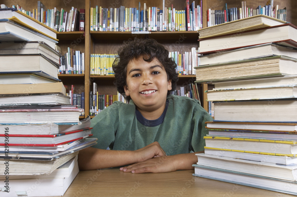Portrait of a happy school boy sitting at desk with stack of books in library Portrait of a happy school boy sitting at desk with stack of books in library