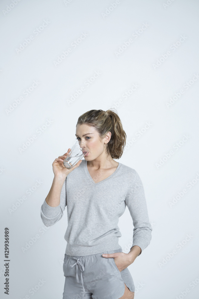 Beautiful young woman with hand in pocket drinking water from glass isolated over colored background Beautiful young woman with hand in pocket drinking water from glass isolated over colored background