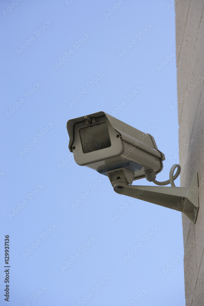 Closeup of a security camera mounted on wall against blue sky Closeup of a security camera mounted on wall against blue sky