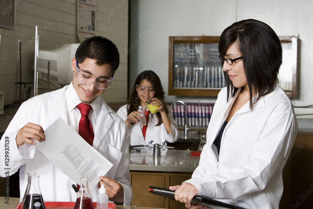 Fototapeta premium High school student holding curriculum paper with professor and classmates in the chemistry lab