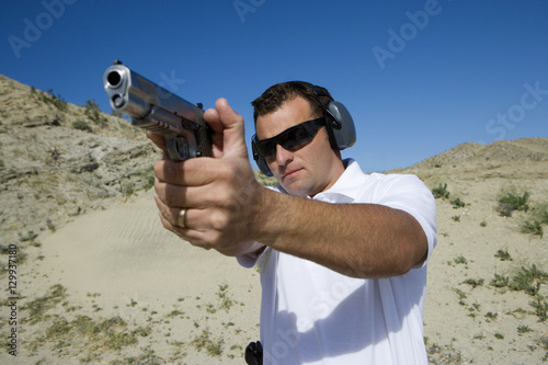 Man aiming the target while holding handgun and mountain in the background