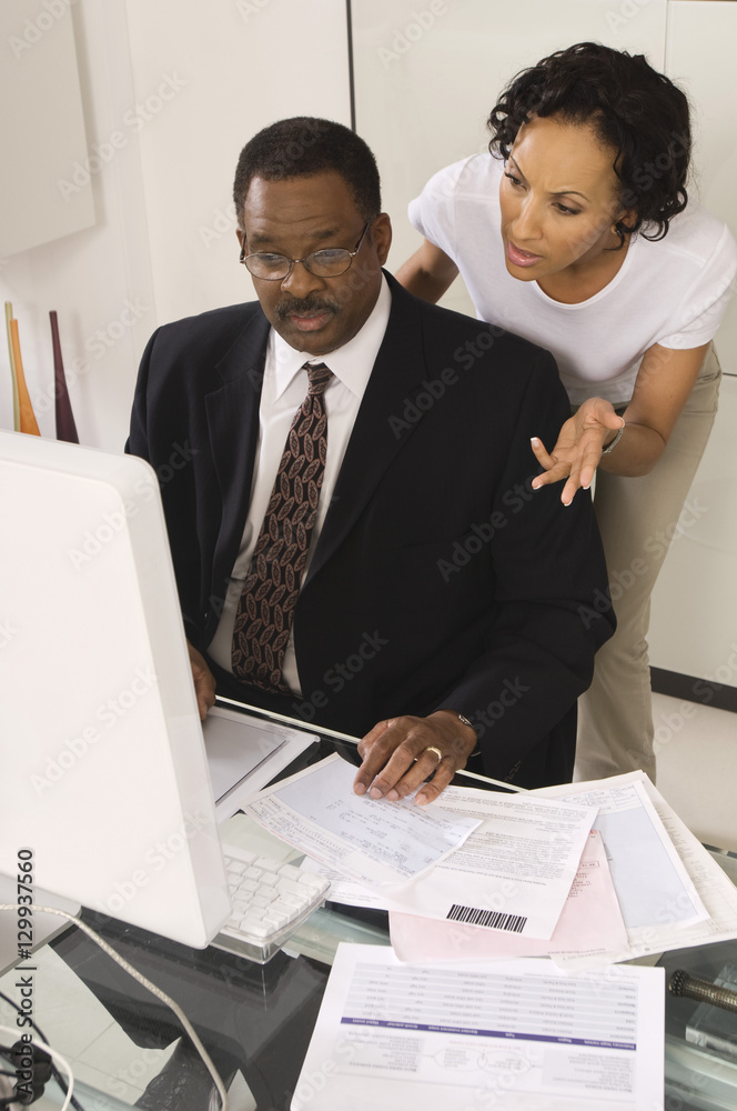 Accountant and female client looking at computer at desk while calculating budget in office Accountant and female client looking at computer at desk while calculating budget in office