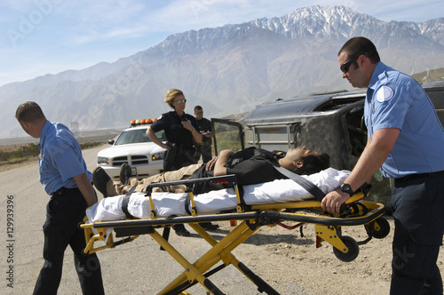 Fotografie Paramedics transporting victim on stretcher with police officers in the backgrou