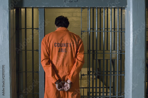 Handcuffed male criminal wearing prison uniform stands in jail Fototapet