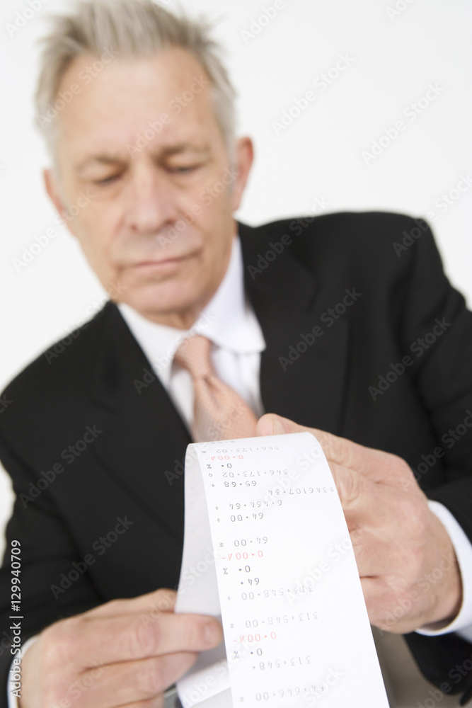 Senior businessman looking at calculator paper tape Senior businessman looking at calculator paper tape