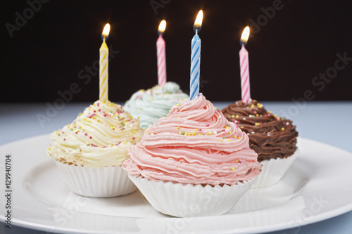 Four cupcakes with lighted candles on plate isolated over black background