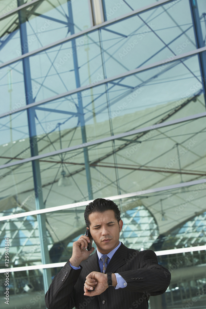 Businessman on call checking out the time outside office building Businessman on call checking out the time outside office building