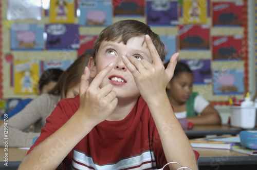 Thoughtful young boy using fingers to count in classroom