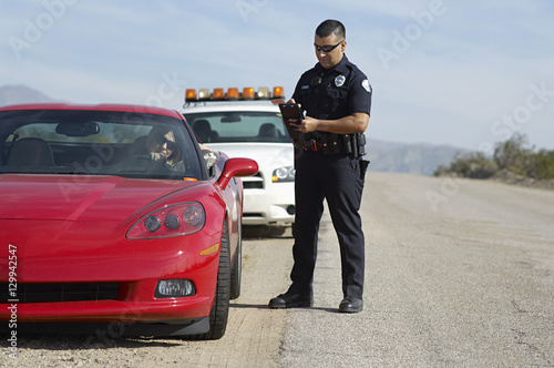 Full length of police officer writing a ticket for woman driving sports car photo