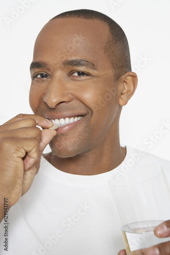 Portrait of an African American man taking pill as he holds glass of water