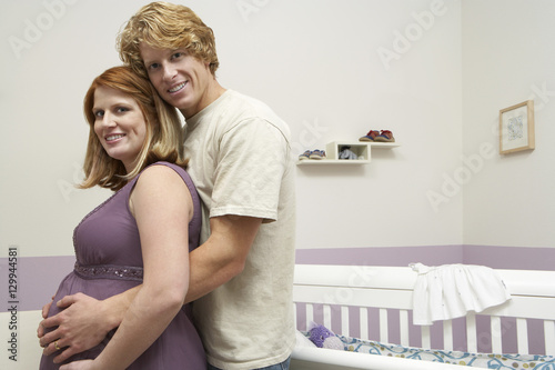 Portrait of happy young expectant couple embracing by cradle photo