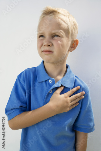Canvas Print Little boy in casual t-shirt standing with hand on heart isolated over white bac