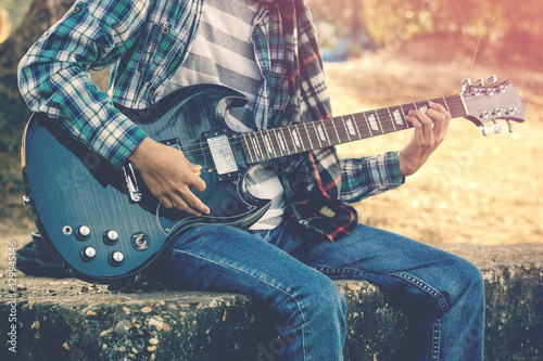 Handsome young man playing guitar in the riverside, enjoy playing guitar.