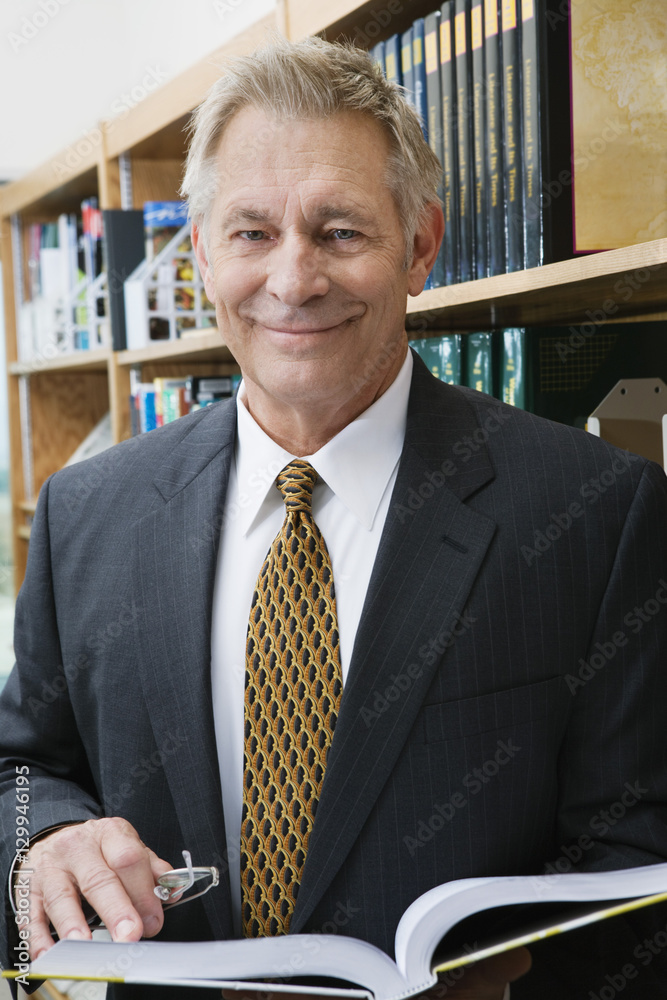 Naklejka premium Portrait of a happy business man standing in library with book
