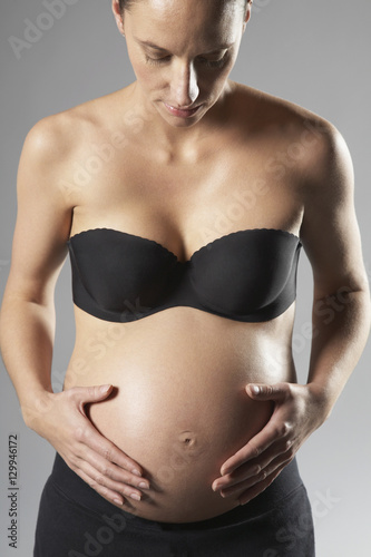 Midsection of pregnant woman touching abdomen on gray background