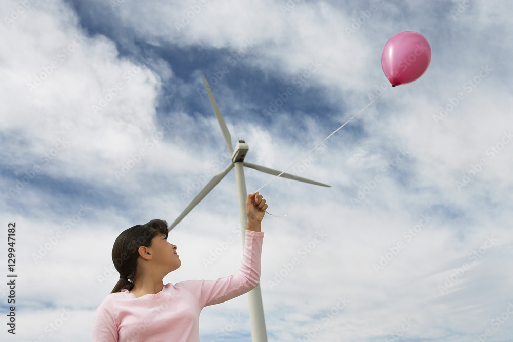 Low angle view of girl playing with pink balloon near turbine at wind farm Low angle view of girl playing with pink balloon near turbine at wind farm