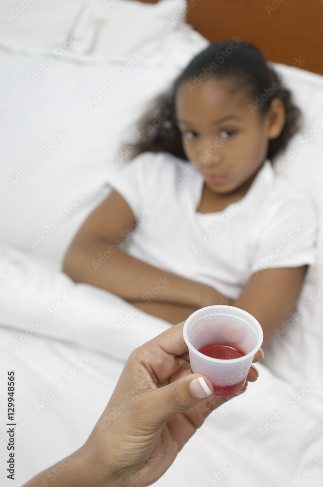 Woman's hand holding medication for girl lying in bed Woman's hand holding medication for girl lying in bed