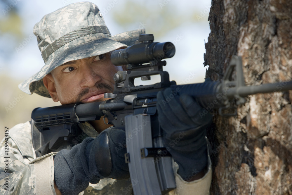 US army soldier aiming with machine gun from behind a tree trunk US army soldier aiming with machine gun from behind a tree trunk