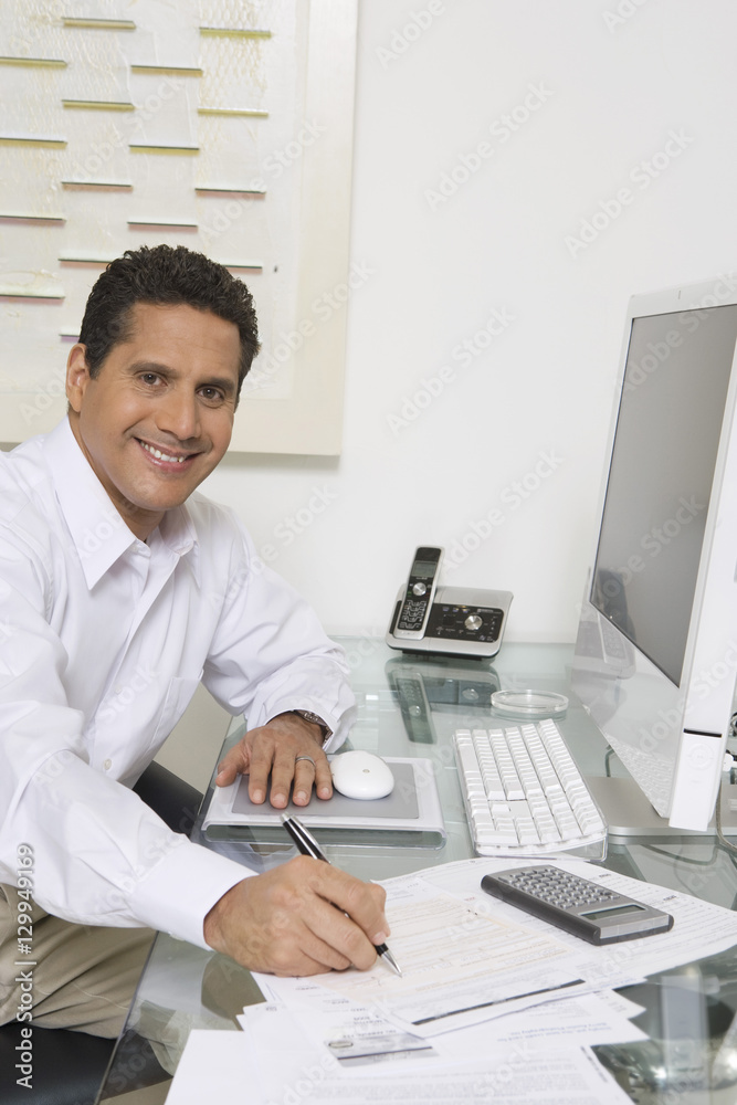 Portrait of a happy businessman at computer desk writing document
