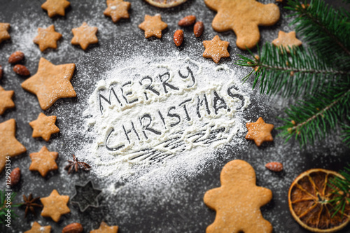 Merry Christmas greeting written on flour. Christmas holidays card with gingerbread cookies, spices, fir tree. Selective focus