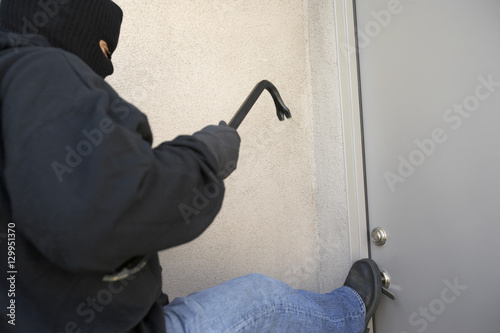 Burglar with crowbar kicking the door of house