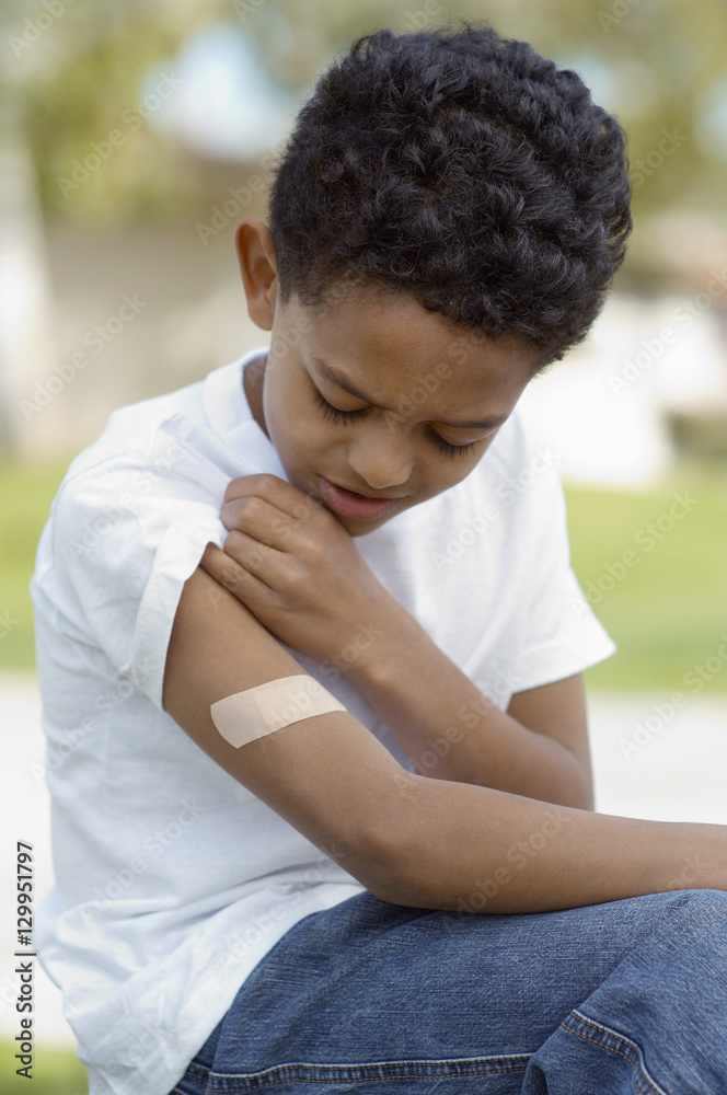 Closeup of an upset young boy looking at bandage on arm Closeup of an upset young boy looking at bandage on arm