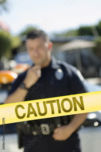 Closeup of a caution tape with male police officer in the background