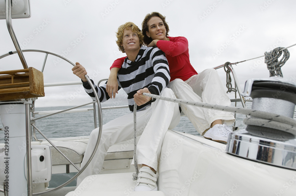 Young Caucasian couple sitting on yacht by helm