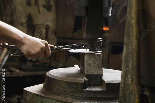 Young male blacksmith shaping metal in workshop