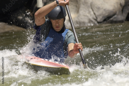 Young man whitewater kayaking on mountain river