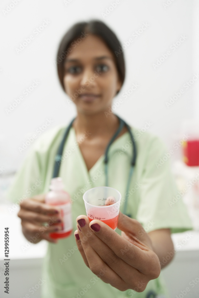 Closeup of young doctor holding out medicine in liquid measure Closeup of young doctor holding out medicine in liquid measure