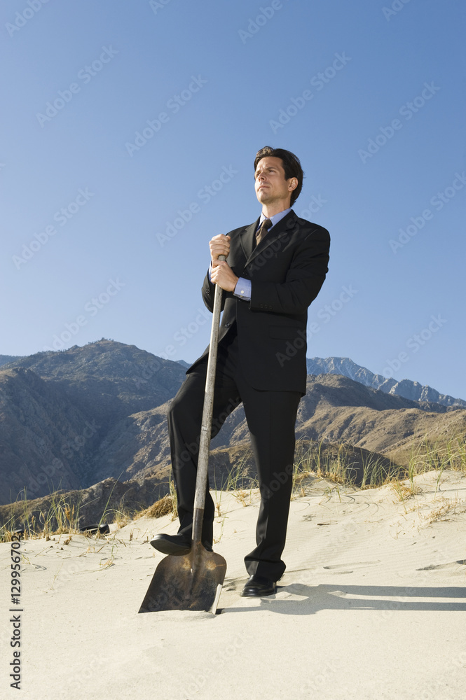 Full length of a businessman standing with spade in the desert on a sunny day