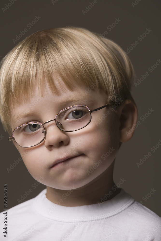 Closeup portrait of a blonde haired boy wearing glasses against gray background Closeup portrait of a blonde haired boy wearing glasses against gray background