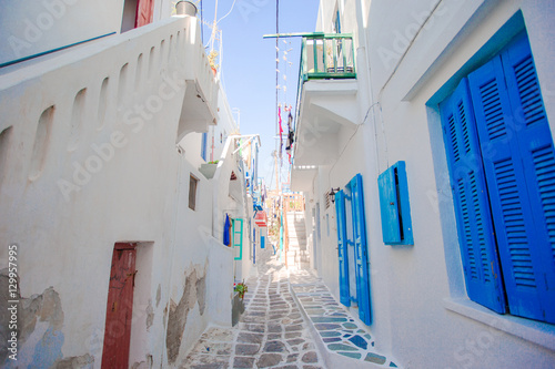 Fototapeta Naklejka Na Ścianę i Meble -  The narrow streets of greek island with blue balconies, stairs and flowers. Beautiful architecture building exterior with cycladic style.