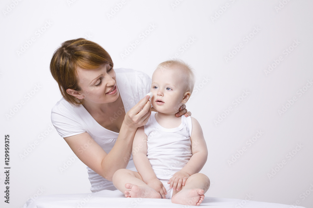 Young woman cleaning baby's face against white background Young woman cleaning baby's face against white background