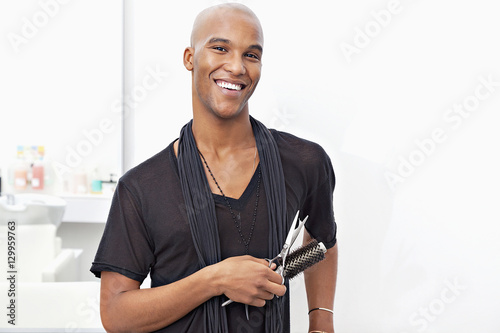 Portrait of happy male stylist holding hairbrush and scissors