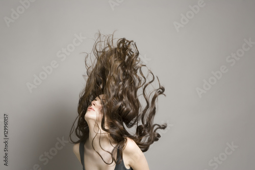 Young woman tossing long brown wavy hair against gray background