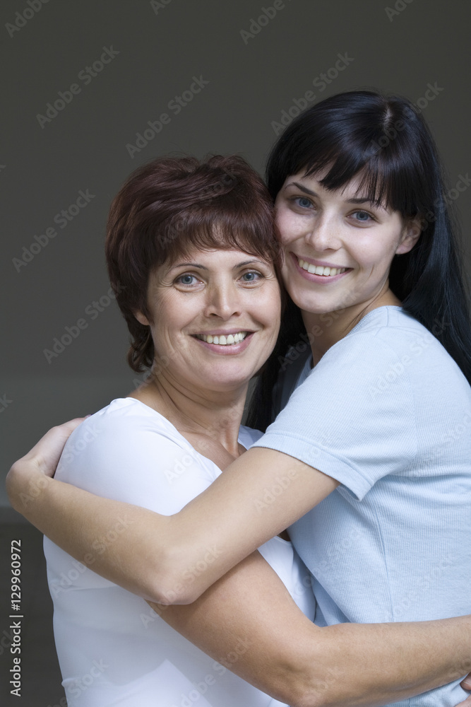 Portrait of a smiling young woman embracing her mother against gray background Portrait of a smiling young woman embracing her mother against gray background