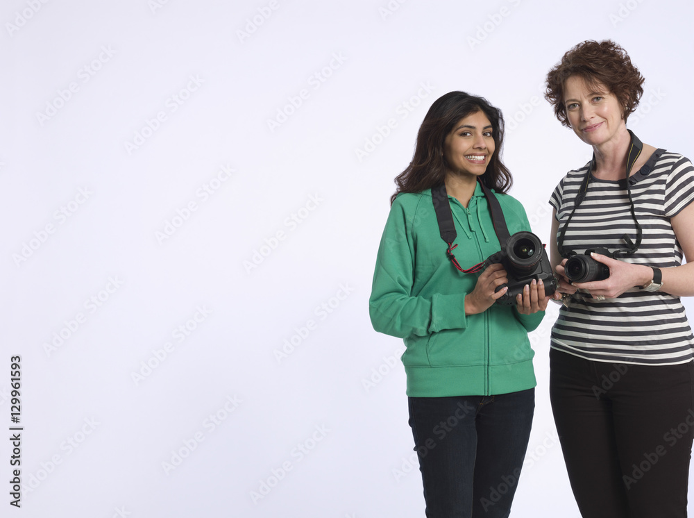 Portrait of two multiethnic women holding digital cameras in studio Portrait of two multiethnic women holding digital cameras in studio