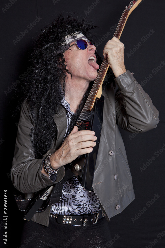 Senior man licking his guitar while performing over black background Senior man licking his guitar while performing over black background